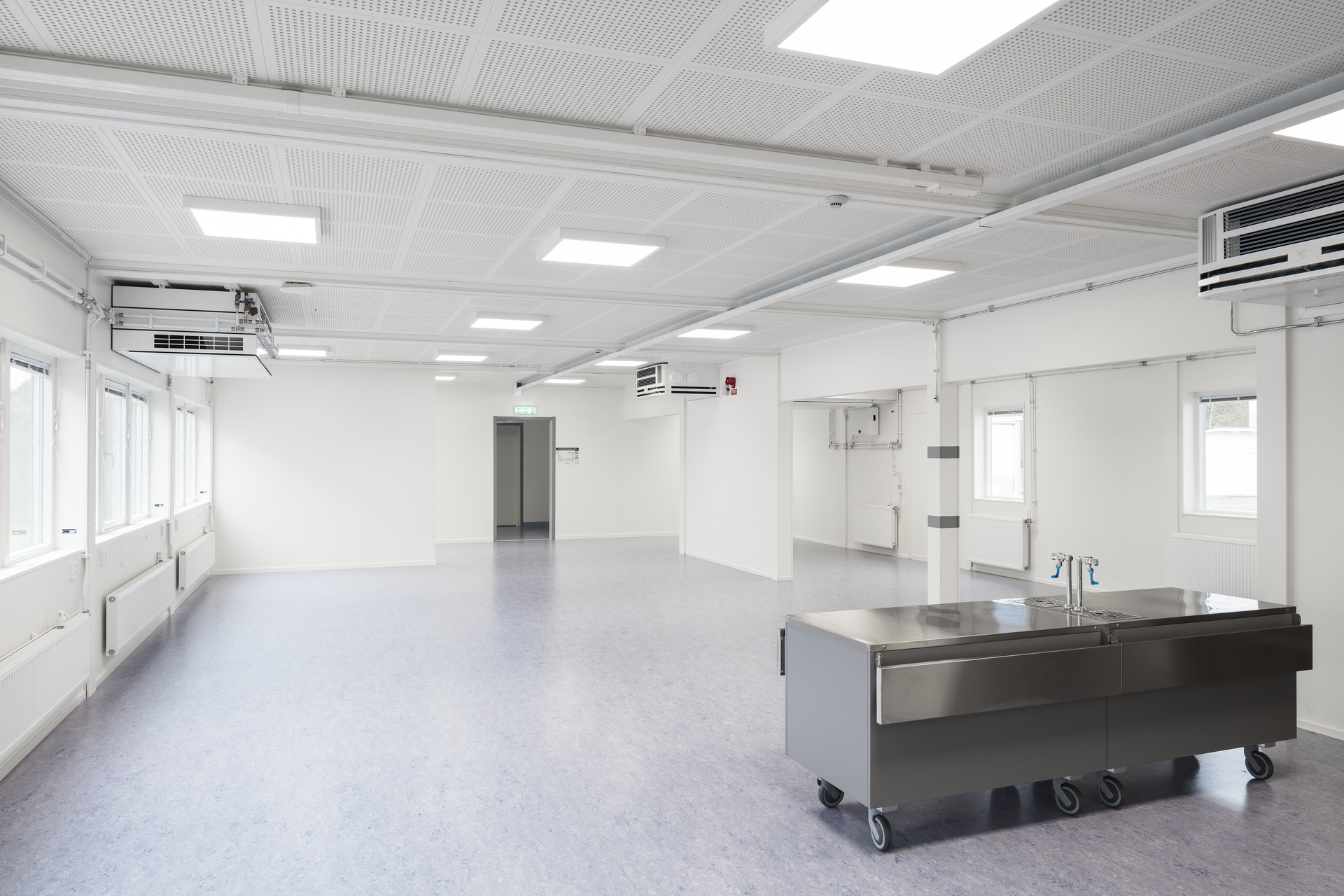 Rymligt och ljust invändigt utrymme i skolans modullösning från Expandia, med stora fönster, god belysning, öppna ytor och en mobil arbetsstation i rostfritt stål anpassad för undervisning och praktiskt arbete.