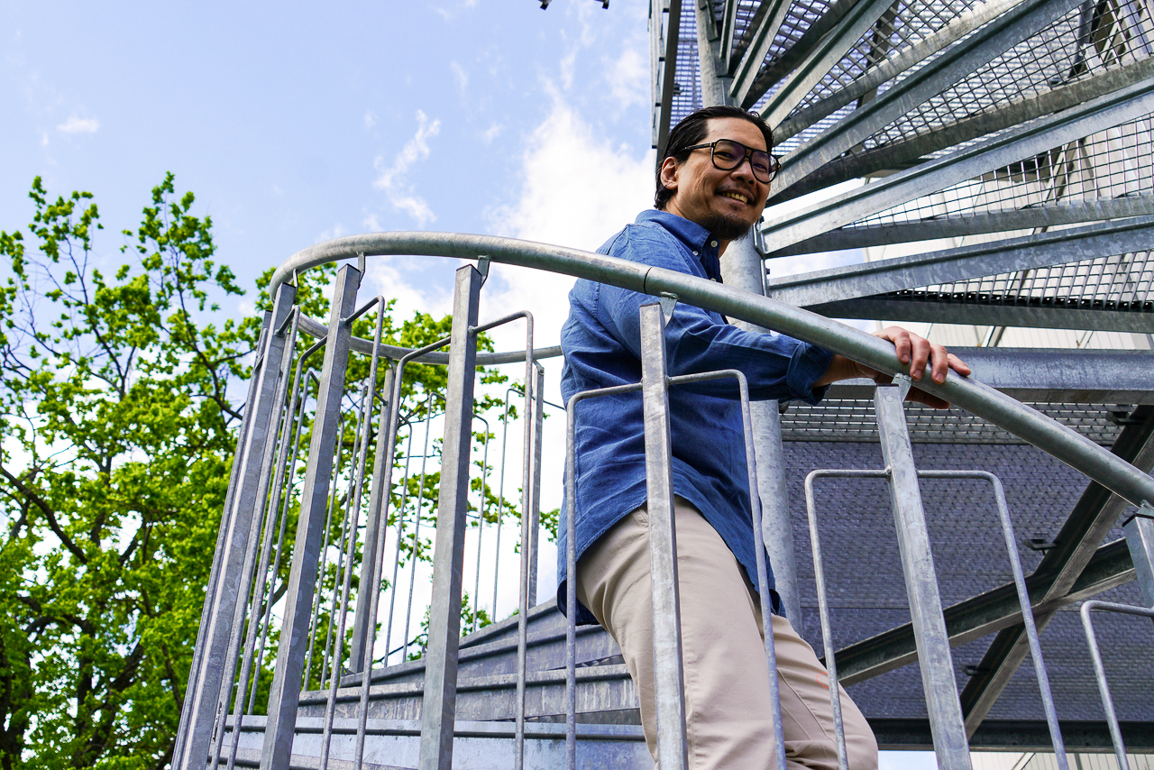 En man går uppför en spiraltrappa i galvaniserat stål utomhus vid modulbyggnaderna på Centralsjukhuset Karlstad. Trappan är en del av kontorsmoduler från Expandia och bilden visar tillgängliga och funktionella utemiljöer med säker åtkomst mellan våningsplan, omgivna av grönska och öppet himlavalv.