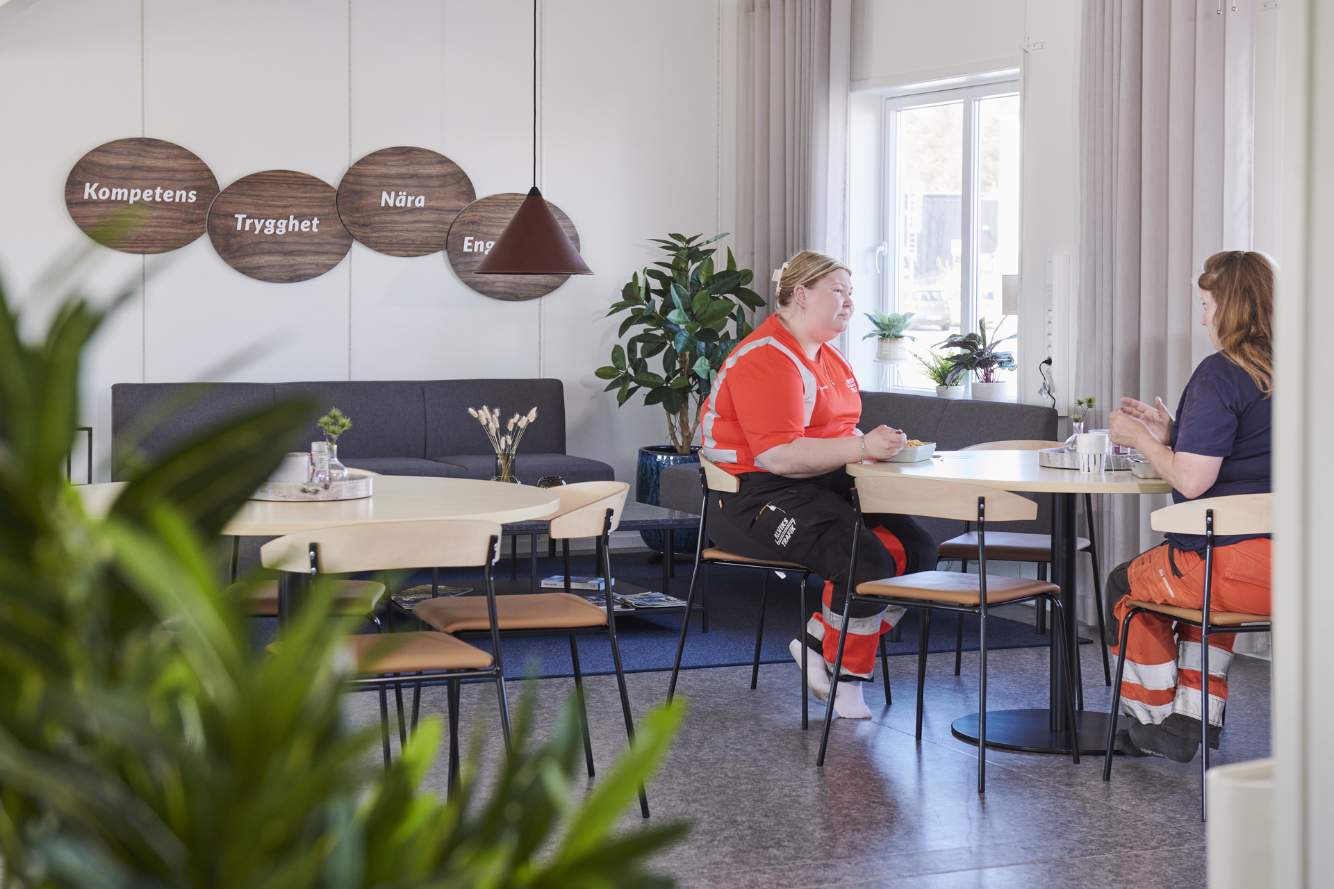 Pausutrymme i kontorsmoduler från Expandia med bord, stolar och soffgrupp i en hemtrevlig miljö. Två personer sitter vid ett bord i samtal, omgivna av växter och inredningsdetaljer. Bilden är tagen i kontorsmoduler vid Alviks trafik i Luleå.
