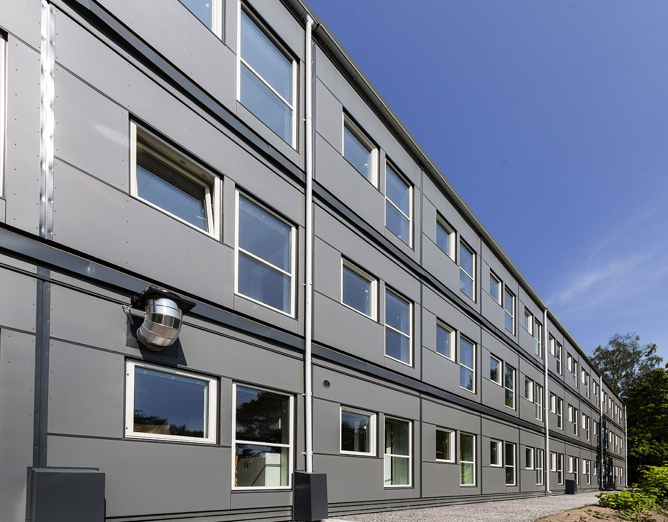 Exteriör vy av skolans modullösning vid Falkbergsskolan i Tullinge, med två våningar av sammanlänkade moduler, stora fönster och grå fasad i en flexibel modullösning från Expandia.