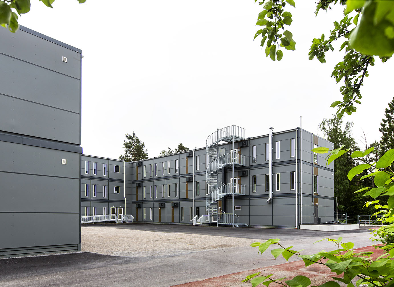 Falkbergsskolan i Tullinge med tre våningar av sammanlänkade grå moduler, utvändigt trapphus och stora fönster, placerad på en öppen skolgård – en flexibel modullösning från Expandia.