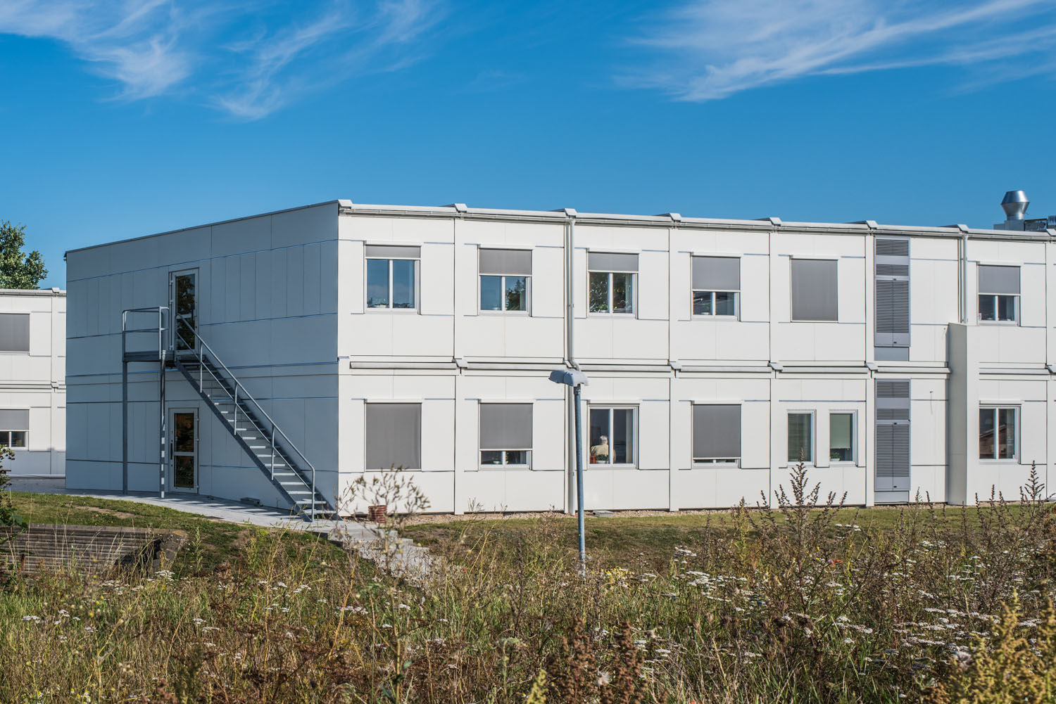 Vita kontorsmoduler i två plan placerade i grön utemiljö. Flexibla kontorsmoduler från Expandia.