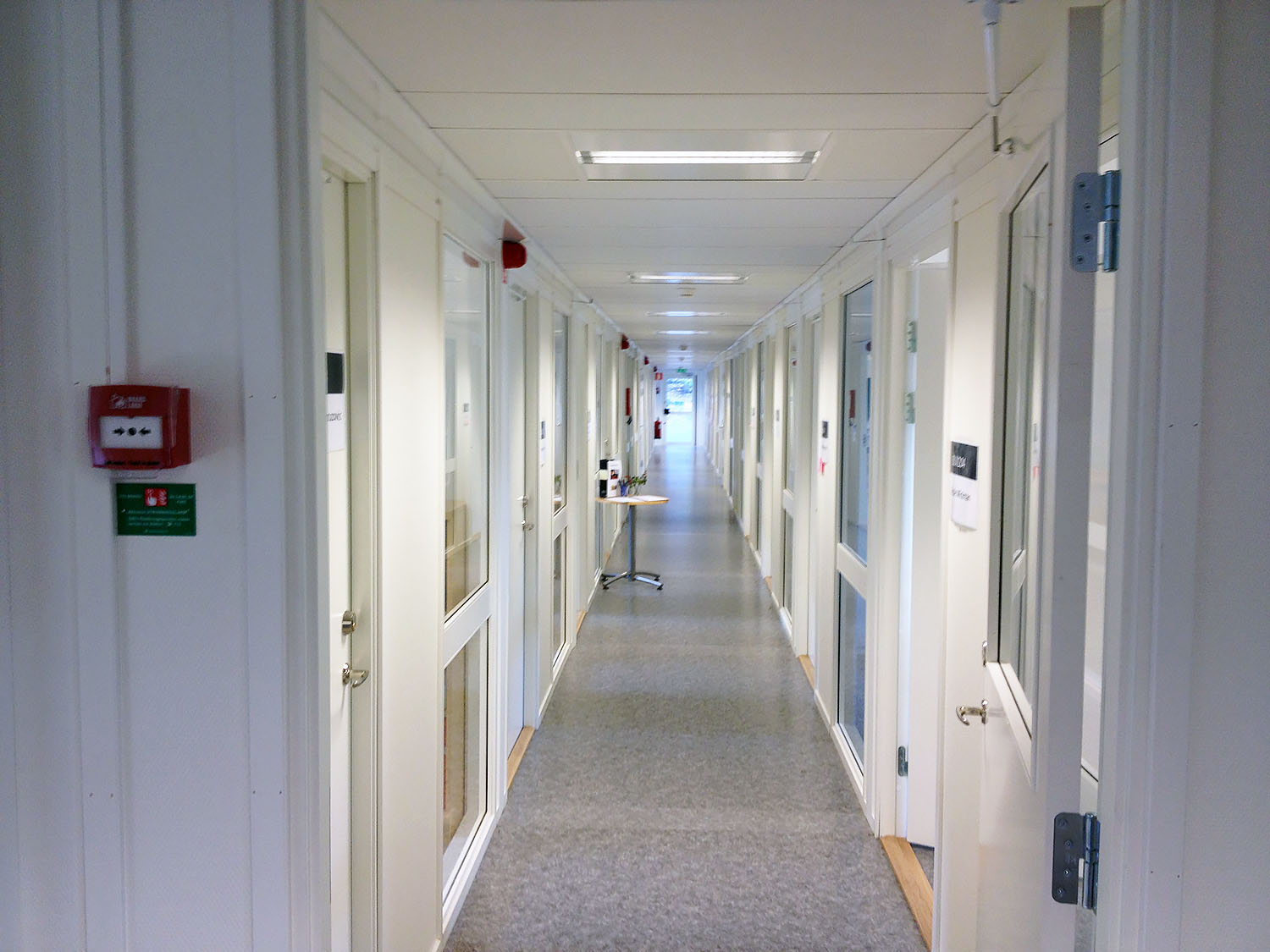 Ljus och lång korridor i kontorsmoduler med kontorsrum på båda sidor, glasade dörrar, heltäckningsmatta och god belysning som skapar en funktionell arbetsmiljö – kontorsmoduler från Expandia.