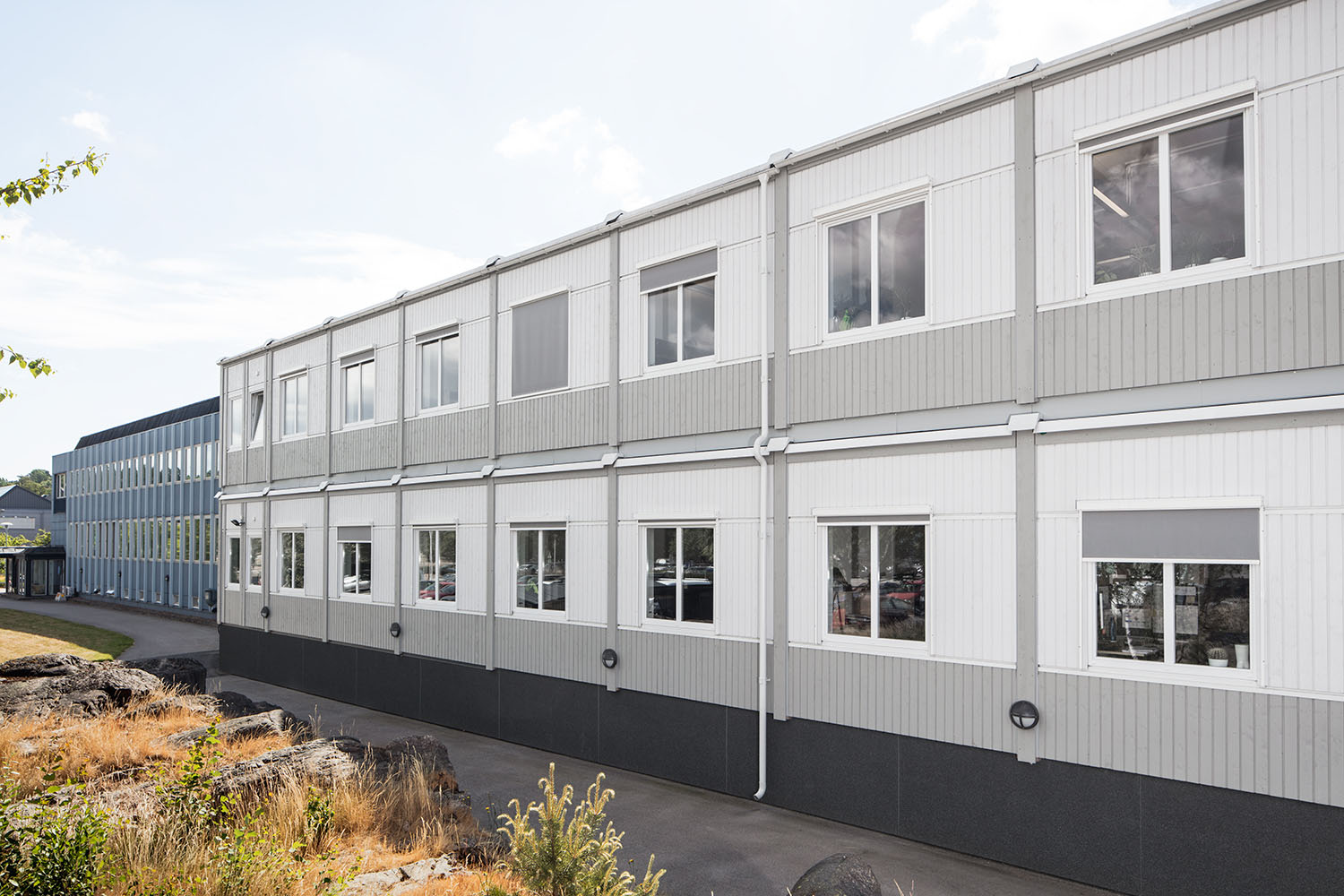 Tvåvånings kontorslösning med ljusgrå fasad och långa fönsterrader, placerad intill gångväg och natur, uppförd med moduler från Expandia.