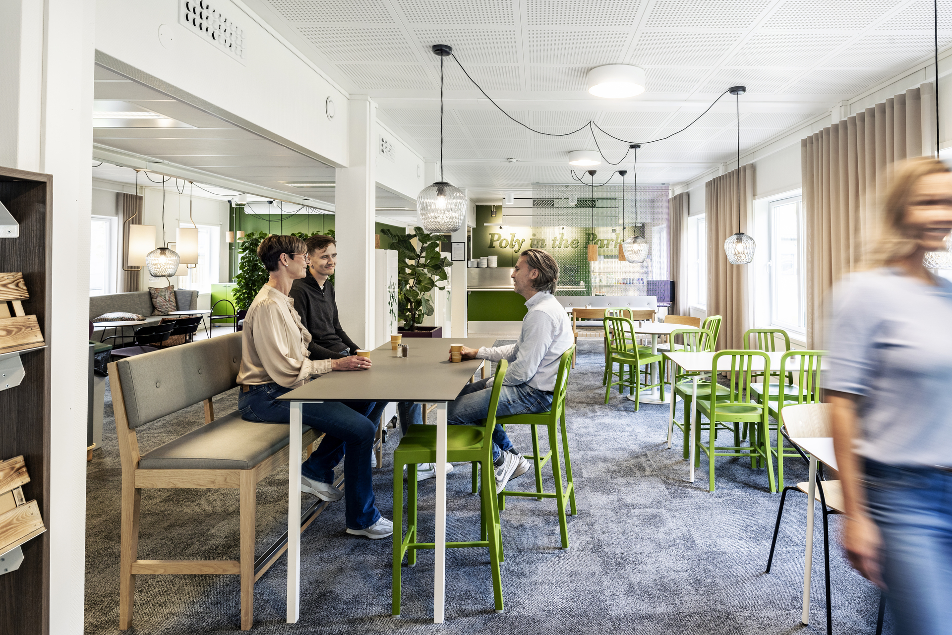 Ljus och modern paus- och mötesyta i kontorsmoduler hos Polypeptide med sittgrupper, höga bord, gröna stolar, växter och mjuk belysning där medarbetare samtalar i en trivsam arbetsmiljö – kontorsmoduler från Expandia.
