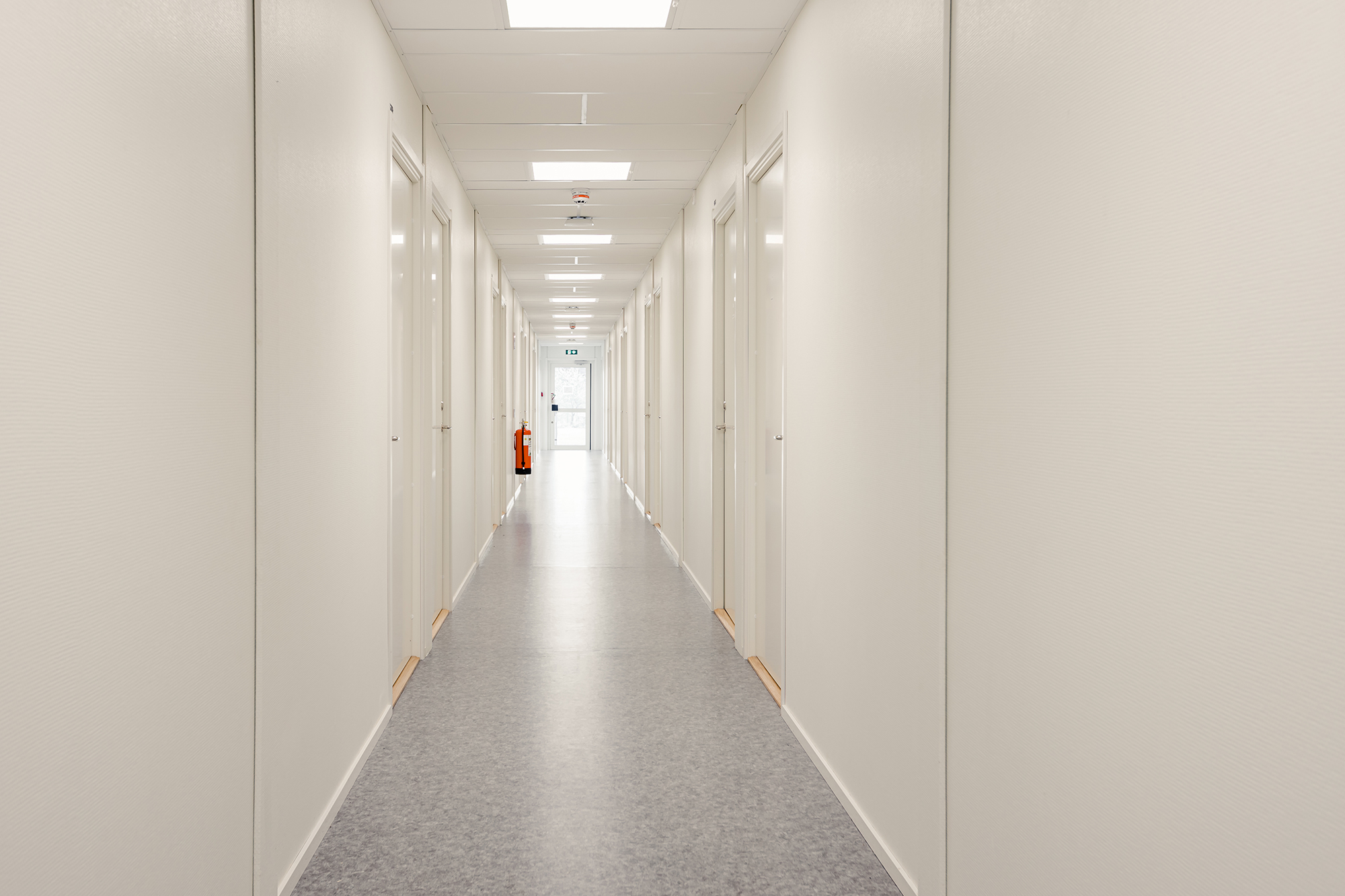 Korridorsboenden med dörrar till boenderum längs båda sidor och utgång längst bort.