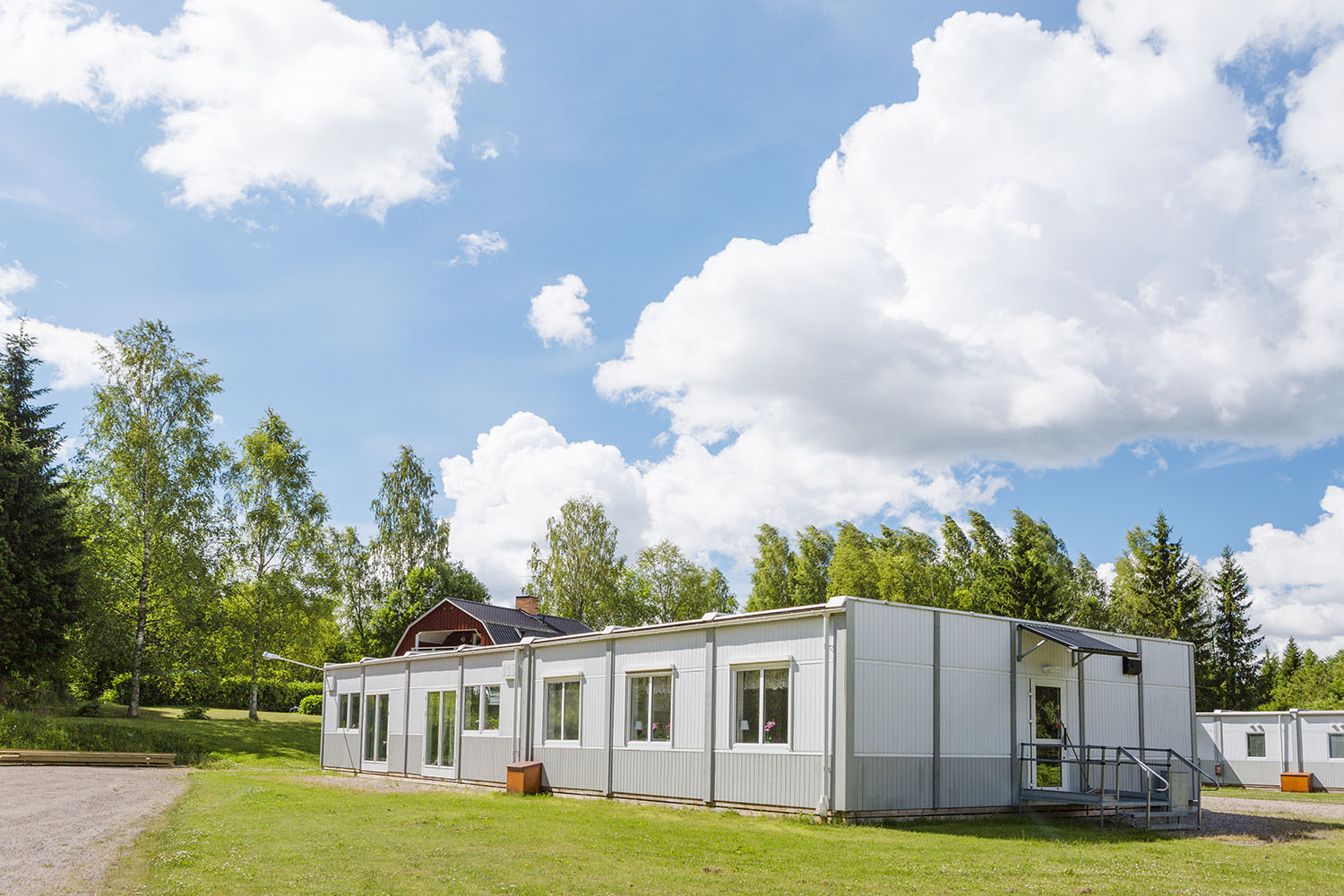 Boendemoduler från Expandia placerade i grön miljö med gräsyta, träd och blå himmel med vita moln.