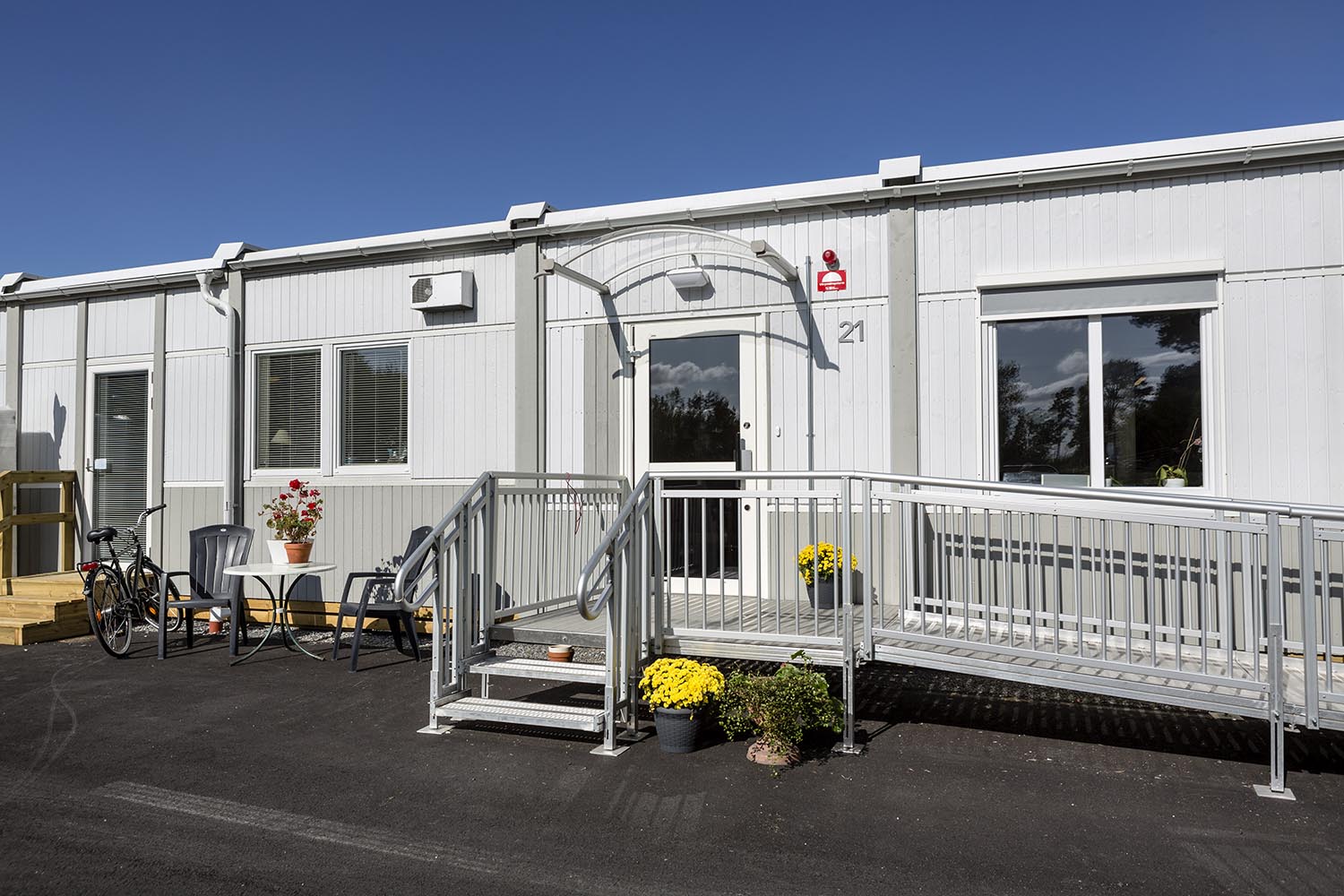 Entré till boendemodul från Expandia vid Nordrona LSS-boende i Norrtälje, med tillgänglig ramp, räcke, uteplats med möbler och blomkrukor.