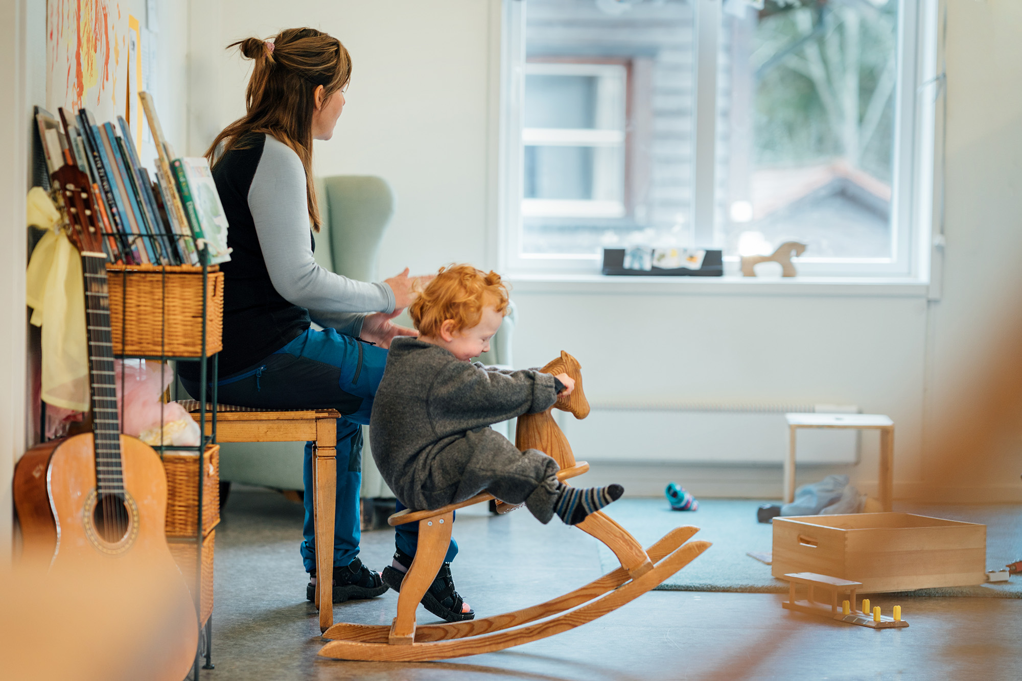 Barn som leker på gyngehest sammen med en ansatt i et lyst og trygt barnehagemiljø i modulbygg fra Expandia.