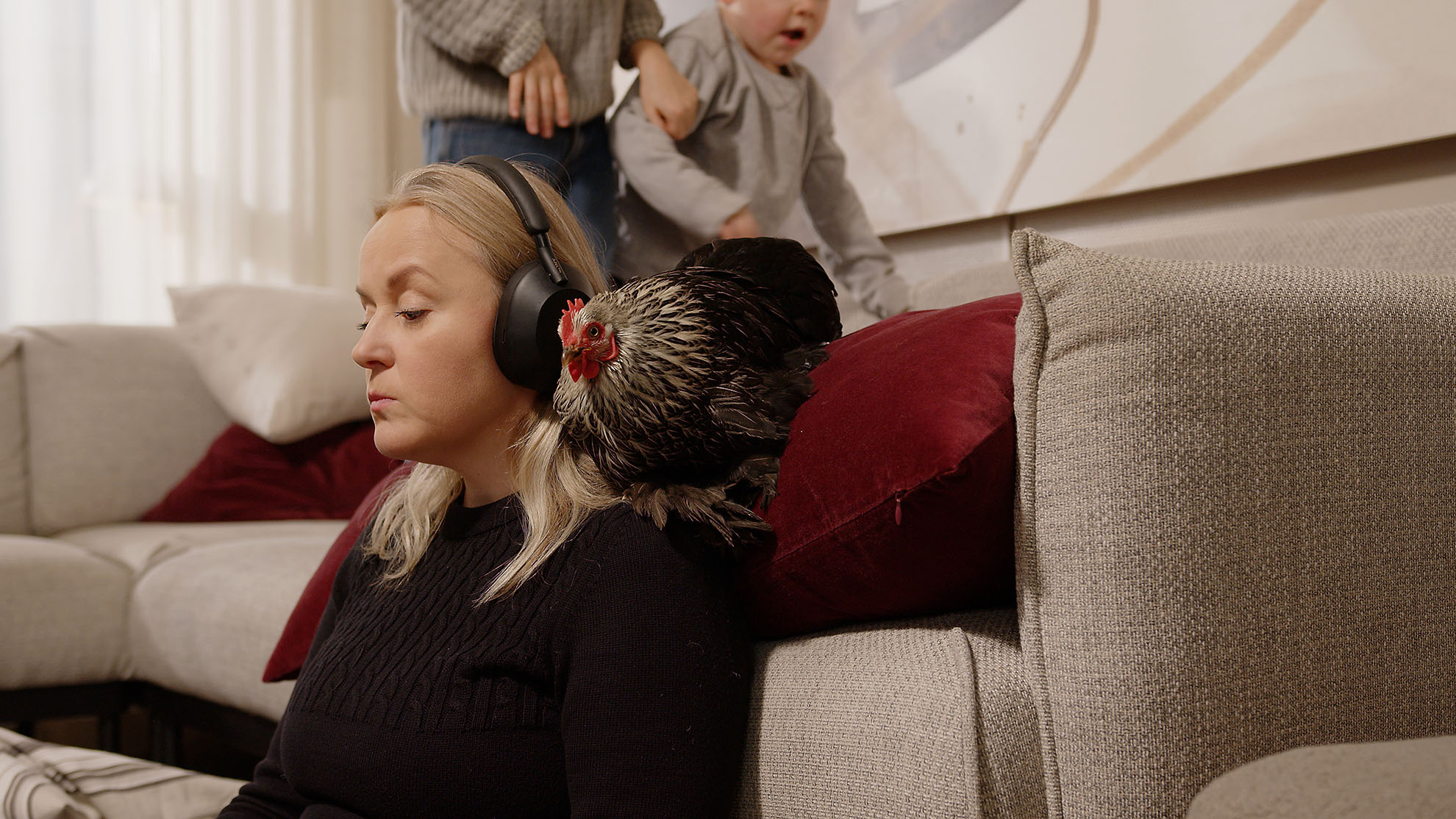 mamma sitter med dator medan barn hoppar i soffan och höna sitter på axeln