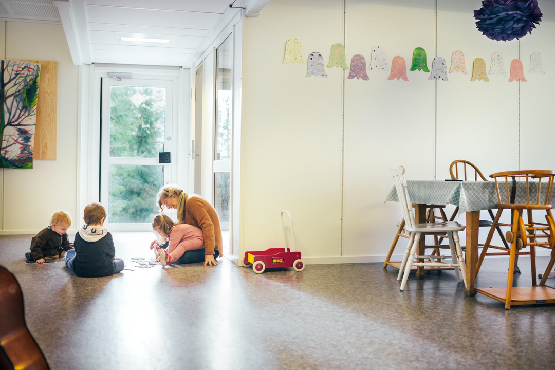 Barn og ansatt i lek på gulvet i et lyst og romslig barnehagemiljø med modulbygg fra Expandia, med god plass til aktiviteter og samspill.