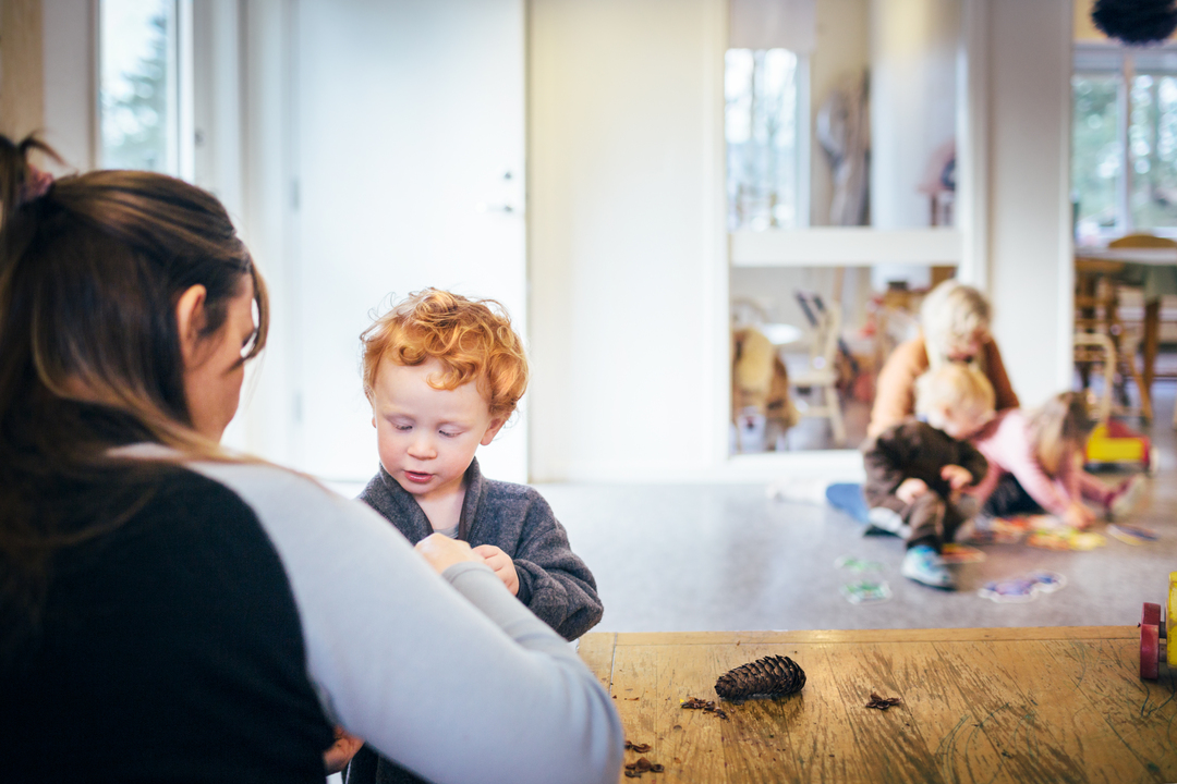 Barn og voksen i samspill i et lyst og trygt barnehagemiljø, med flere barn i lek i bakgrunnen i modulbygg fra Expandia.